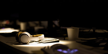 Headphones resting on a modern desk with a keyboard, mouse, and monitor, illuminating a focused workspace ambiance, representing late night work, music, or concentrated study in a quiet home officeの素材
