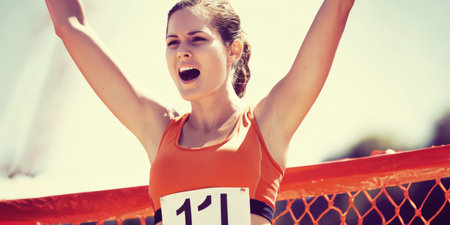 Young woman raising arms in triumph at finish line, celebrating a race victory with determination and exhilaration, embodying athletic achievement, strength and joy outdoorsの素材