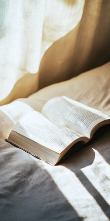 Open book on a cozy bed bathed in warm morning sunlight, casting soft shadows across pages and linens, evoking calm, quiet reading and relaxed weekend solitudeの素材