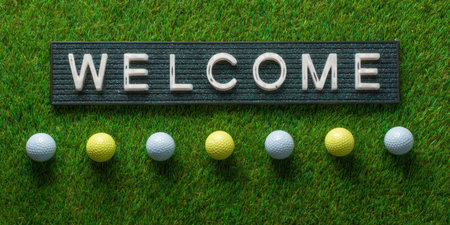 Welcome sign spelled on a board on lush golf-course turf with a row of assorted golf balls, conveying invitation, leisure and sporting celebration in a top-view compositionの素材