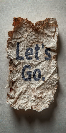 Crumpled and burnt-edged paper with the encouraging message let's go on a textured canvas background, symbolizing motivation, challenge, and opportunity for a new startの素材