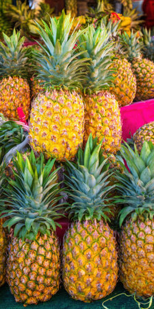 Ripe pineapples with vibrant green crowns stacked at an outdoor market stall, showcasing fresh tropical produce ready for selling, healthy eating, and summer snacksの素材