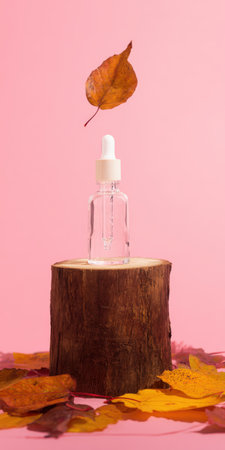 Clear cosmetic dropper bottle with natural serum standing on a wooden pedestal, surrounded by fall leaves, representing natural beauty and seasonal skin careの素材