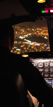 Pilot is sitting in the cockpit of an airplane, looking over the cityscape illuminated with bright lights from above during a nighttime flight, emphasizing journey and perspectiveの素材