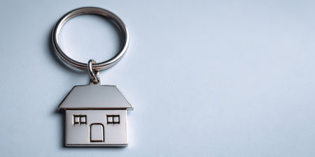 House-shaped metal key ring representing real estate, property ownership, buying a new home, and investment in the housing market, placed on a light background with copy spaceの素材