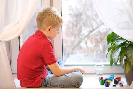 Young boy feeling bored looking out windowの写真素材
