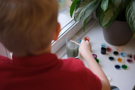 Child painting watercolors on windowsill for creative hobbyの写真素材