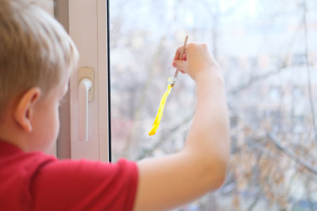 Young child painting yellow stripe on window glassの写真素材