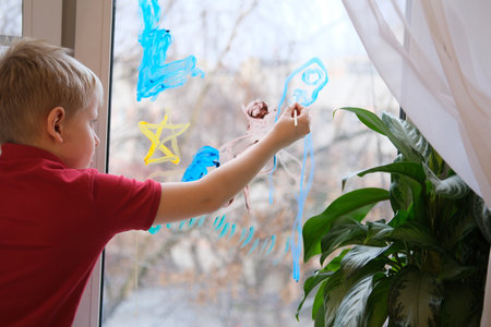 Young boy drawing on window with colorful paintの写真素材
