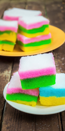 Kue lapis cakes featuring colorful layers of white, pink, green, yellow, and blue, representing traditional Indonesian sweet treats on a rustic wooden tableの素材