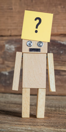 Wooden robot with metal eyes and a question mark on a yellow sticky note on its head is standing against a rustic wooden background, symbolizing confusion, doubt, and inquiry in ai and technologyの素材