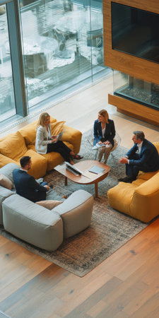 Four business professionals are collaborating in a contemporary office lounge, sitting on comfortable sofas and sharing ideas during a casual team discussion in a stylish workspaceの素材