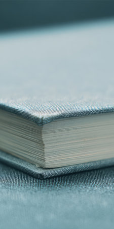 Book with gray cover and many pages resting on a textured fabric surface, representing education, learning, literature, and the pursuit of knowledge in a minimalist setting with ample copy spaceの素材
