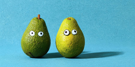 Two funny anthropomorphic avocados with googly eyes stand side by side on a vibrant blue background, playful and lighthearted, evoking friendship, individuality, and healthy funの素材