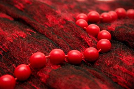 Red beads lay on a woolen female scarf.