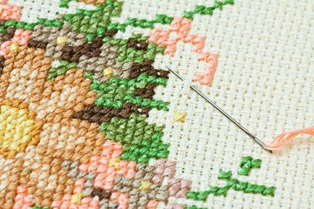 Closeup of needle put into cross-stitch embroidery.