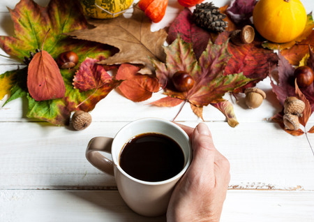 White wooden table with a decor of autumn leaves and a cup of coffee.の写真素材
