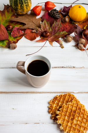 Cup of coffee and wafers on wooden table with autumn leaves.の写真素材