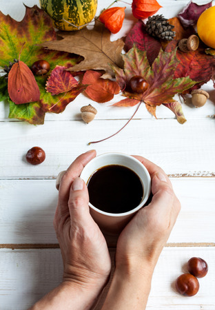 White wooden table with a decor of autumn leaves and a cup of coffee.の写真素材