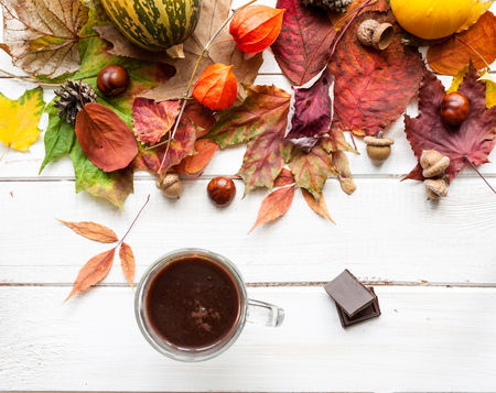 White wooden table with a decor of autumn leaves and a cup of hot chocolate.の写真素材
