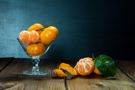 Tangerines (mandarins, citrus fruits) with leaves in glass on rustic wooden background. Still life with space for text.の写真素材