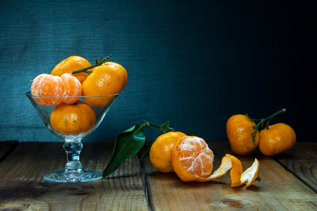 Tangerines (mandarins, citrus fruits) with leaves in glass on rustic wooden background. Still life with space for text.の写真素材