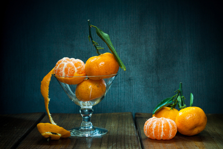 Tangerines (mandarins, citrus fruits) with leaves in glass on rustic wooden background. Still life with space for text.の写真素材
