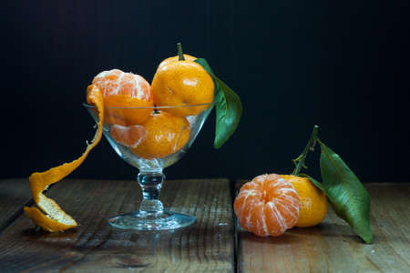 Tangerines (mandarins, citrus fruits) with leaves in glass on rustic woodenの写真素材