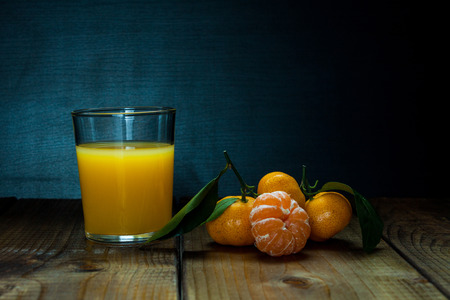 Glass of orange juice and tangerines with leaves on rustic woodenの写真素材