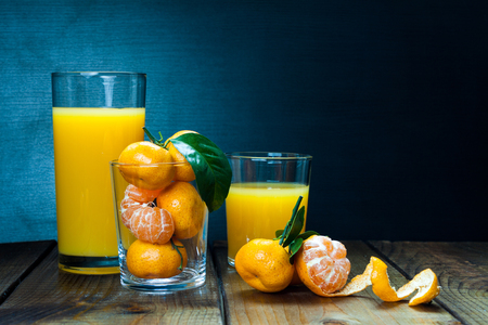 Glass of orange juice and tangerines with leaves on rustic woodenの写真素材