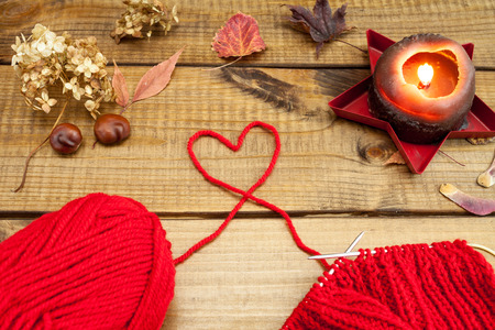 Red knitting wool, knitting needles and dried leaves on woodenの写真素材