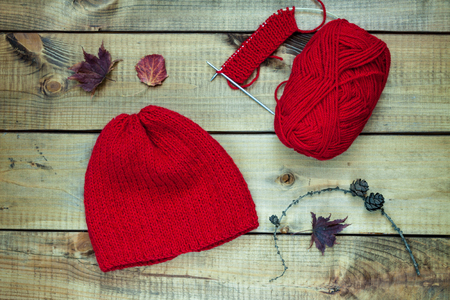 Red knitting wool, knitting needles and dried leaves on woodenの写真素材