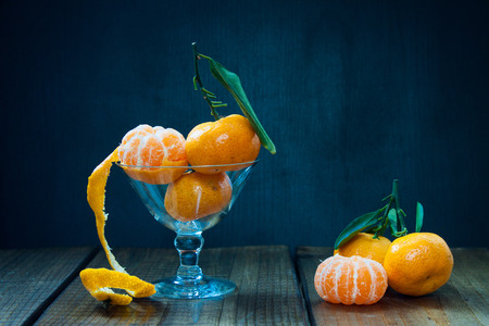 Tangerines (mandarins, citrus fruits) with leaves in glass on rustic woodenの写真素材