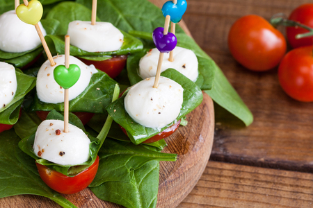 Refreshment with cherry tomatoes, mozzarella and spinach on a wooden board.の写真素材
