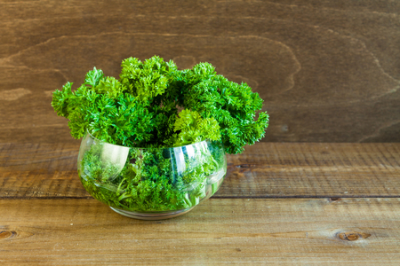 Parsley bunch in a glass bowl on a wooden background.の写真素材