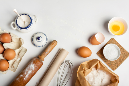 Top view with kitchen tools and ingredients for cake or cookies: flour, egg, sugar on white background. Copy space.の写真素材