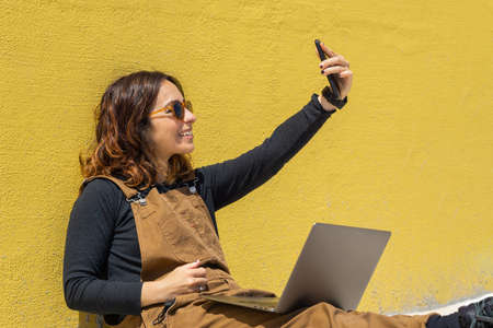 Woman with red headphones sitting on stairs on the street on a sunny day looking at the phone.
