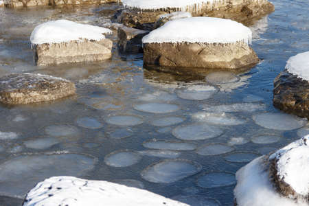 Sea shore in winter, covered with ice and snow. Round ice floes floating in sea water.