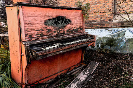 Old broken red piano with peeled paint from rain and wind, outside on an autumn day. Discarded unnecessary musical instrument.のeditorial素材