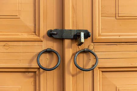 Wooden door with wrought iron handles, closed with a steel bolt with a lock.の写真素材