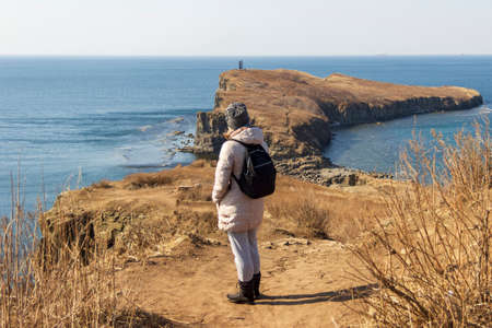 A young woman admires a beautiful view of the sea and rocks at Cape Tobizin on the Russky Island in...
