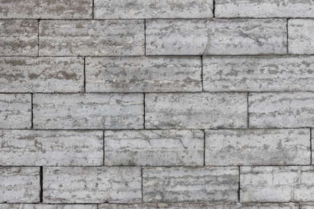 The texture of a gray stone wall made of rectangular marble blocks. Sunlight on the masonry.