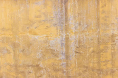 Shabby wall of an old house with uneven crumbling plaster. Yellow-gray abstract texture.