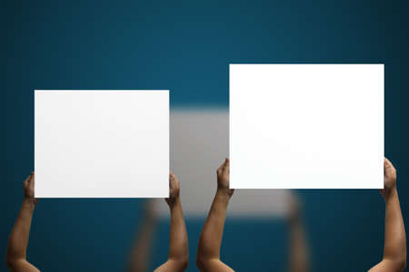 Two separate hands lift white rectangular canvas, one high and one low, in the background of deep blueの写真素材