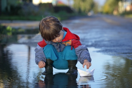 a little boy playing paper ship on a puddle of waterの写真素材