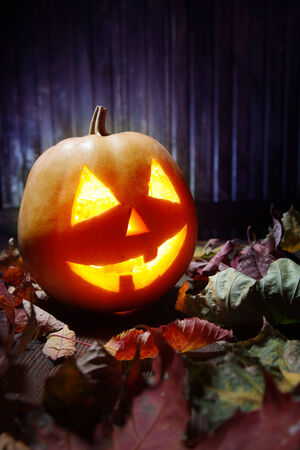 Jack o lanterns  Halloween pumpkin face on wooden background and autumn leafsの写真素材