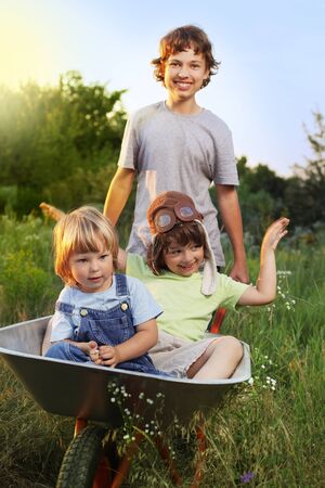 three friends playing in the plane using a garden carts (focus only on child in cart)の写真素材