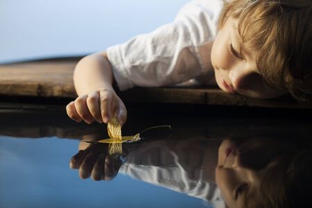 boy play with leaf ship in water (focus on ship)の写真素材