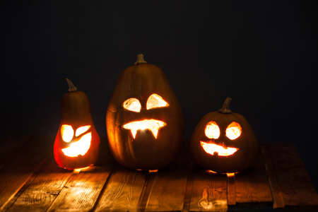 Jack o lanterns Halloween pumpkin face on wooden background and autumn leafsの写真素材