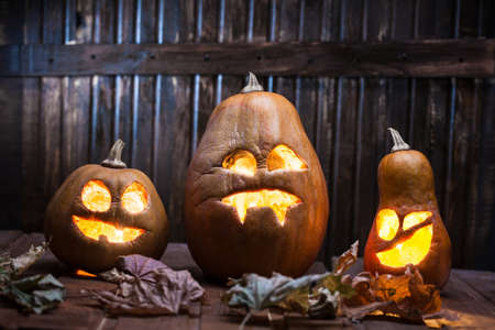 Jack o lanterns Halloween pumpkin face on wooden background and autumn leafsの写真素材